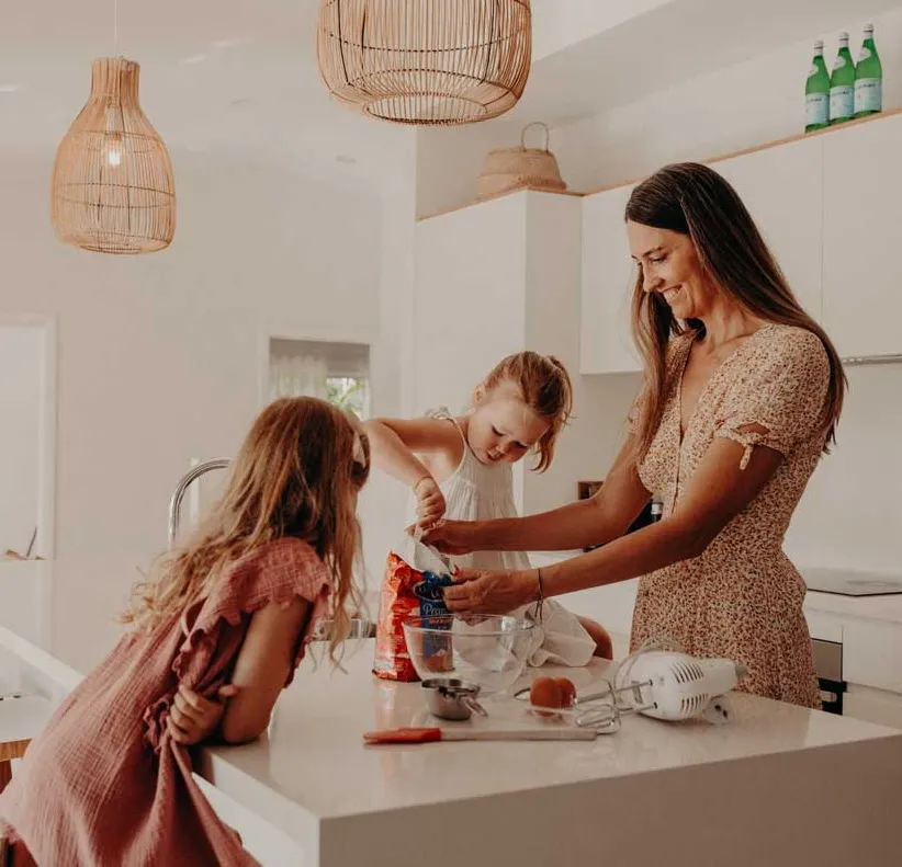 Woman and two girls baking together in a kitchen with mixing bowl and utensils on the counter.