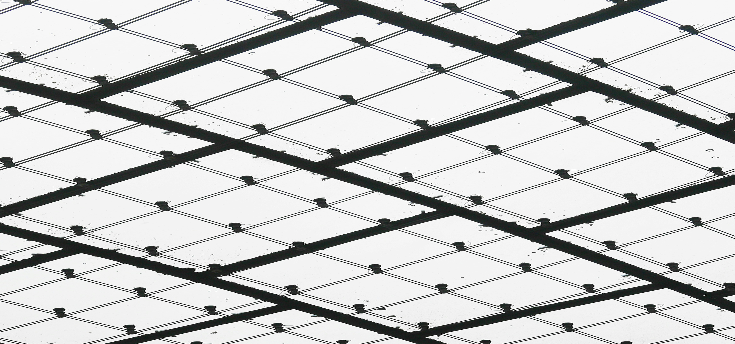 Close-up view of a transparent glass ceiling supported by a black metal grid structure with raindrops on the glass.