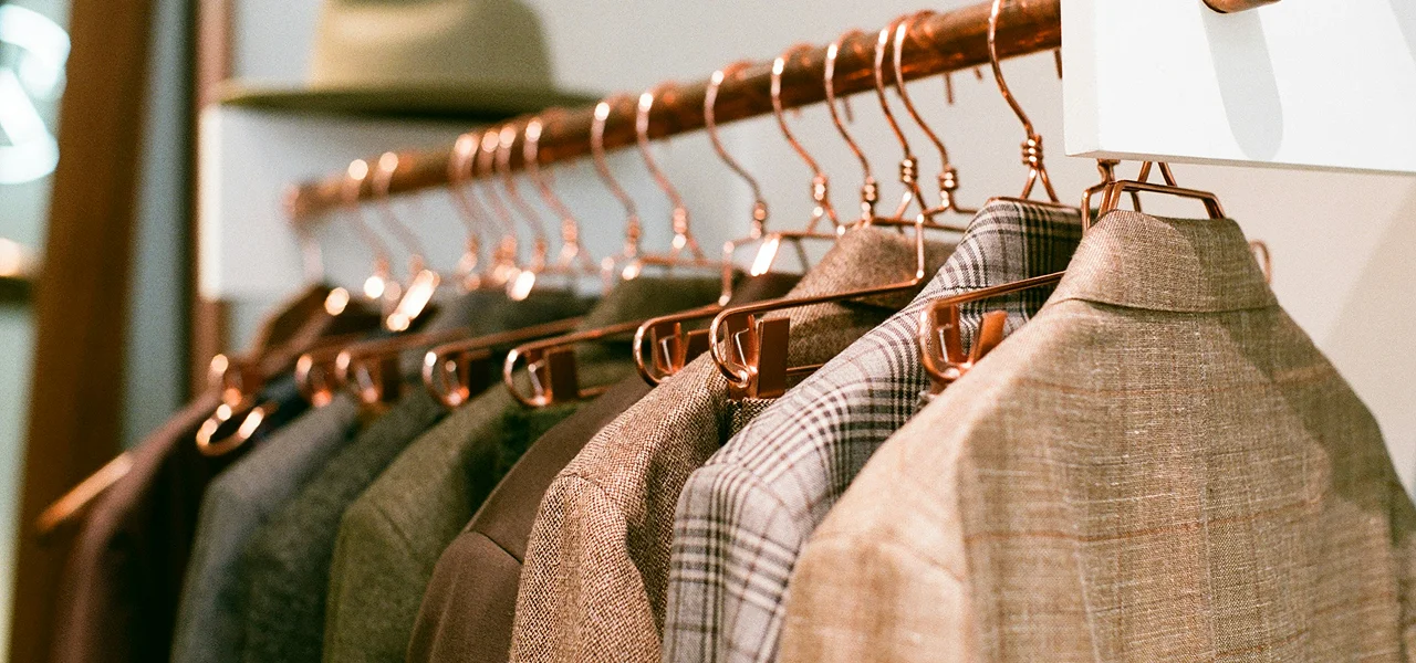 Close-up of formal jackets and blazers in various neutral colors hanging on copper clothing racks in a clothing store.