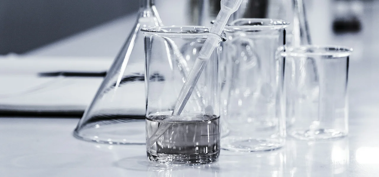 Close-up of transparent glass beakers and laboratory glassware containing clear liquid on a white laboratory surface.