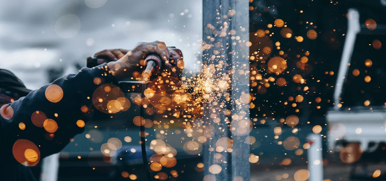 Close-up of a worker using a power tool, with bright orange sparks flying in a dark industrial workshop.