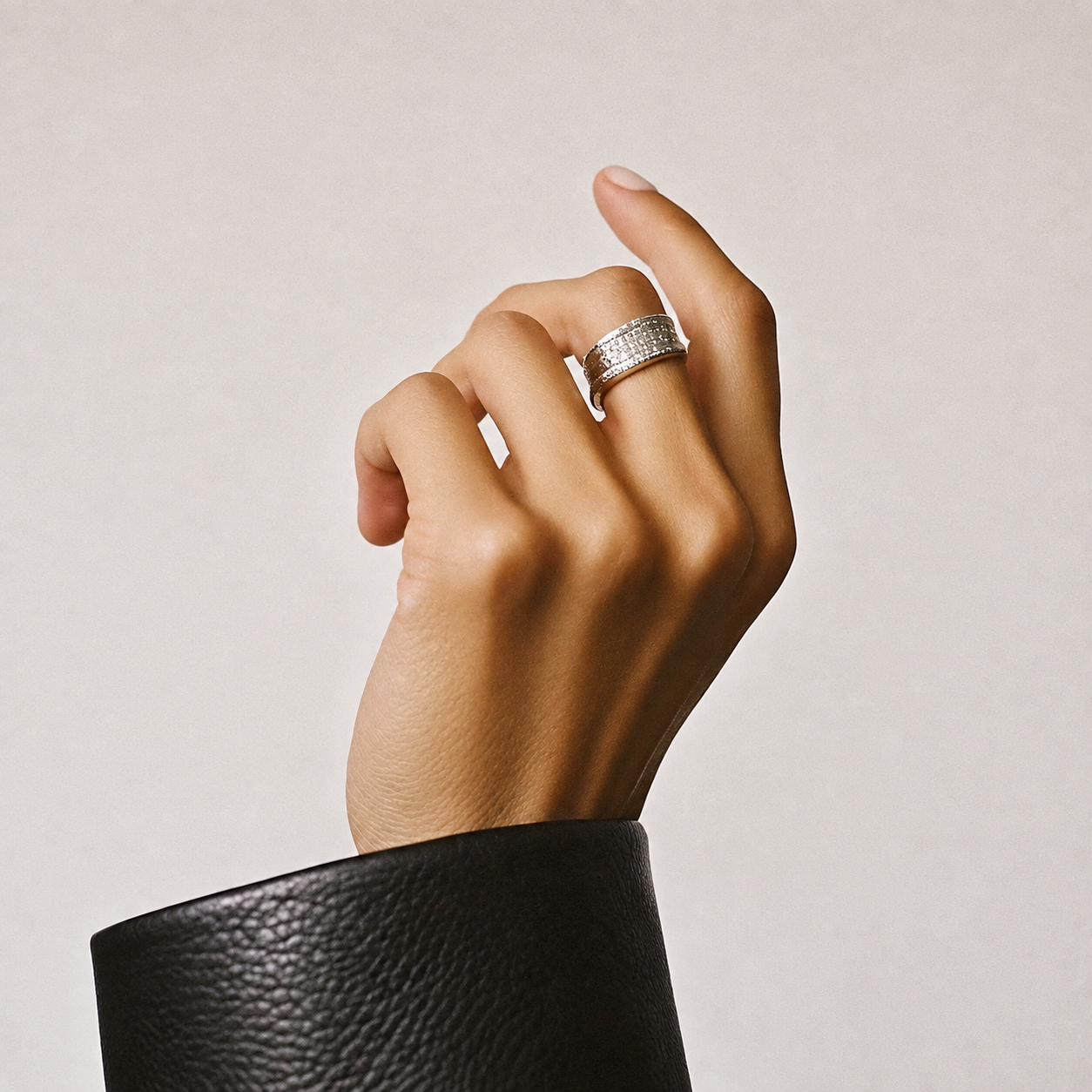 Close-up of a hand with a wide silver ring featuring multiple small embedded stones, wearing a textured black sleeve against a neutral background.