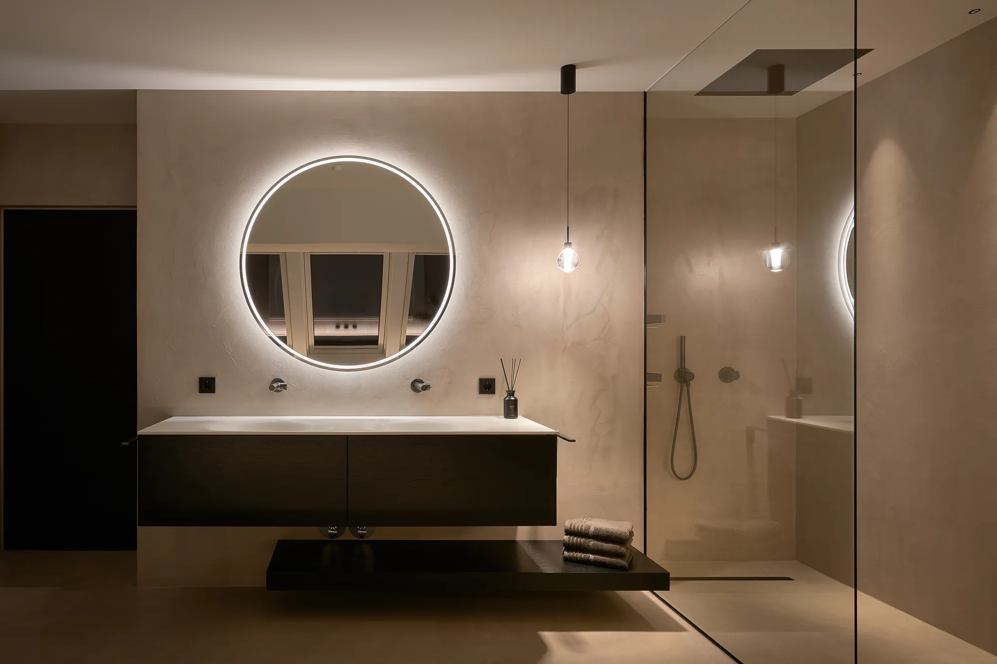 Badezimmer mit durchgehender Spachteltechnik an Wand und Boden, rundem Spiegel und Dusche