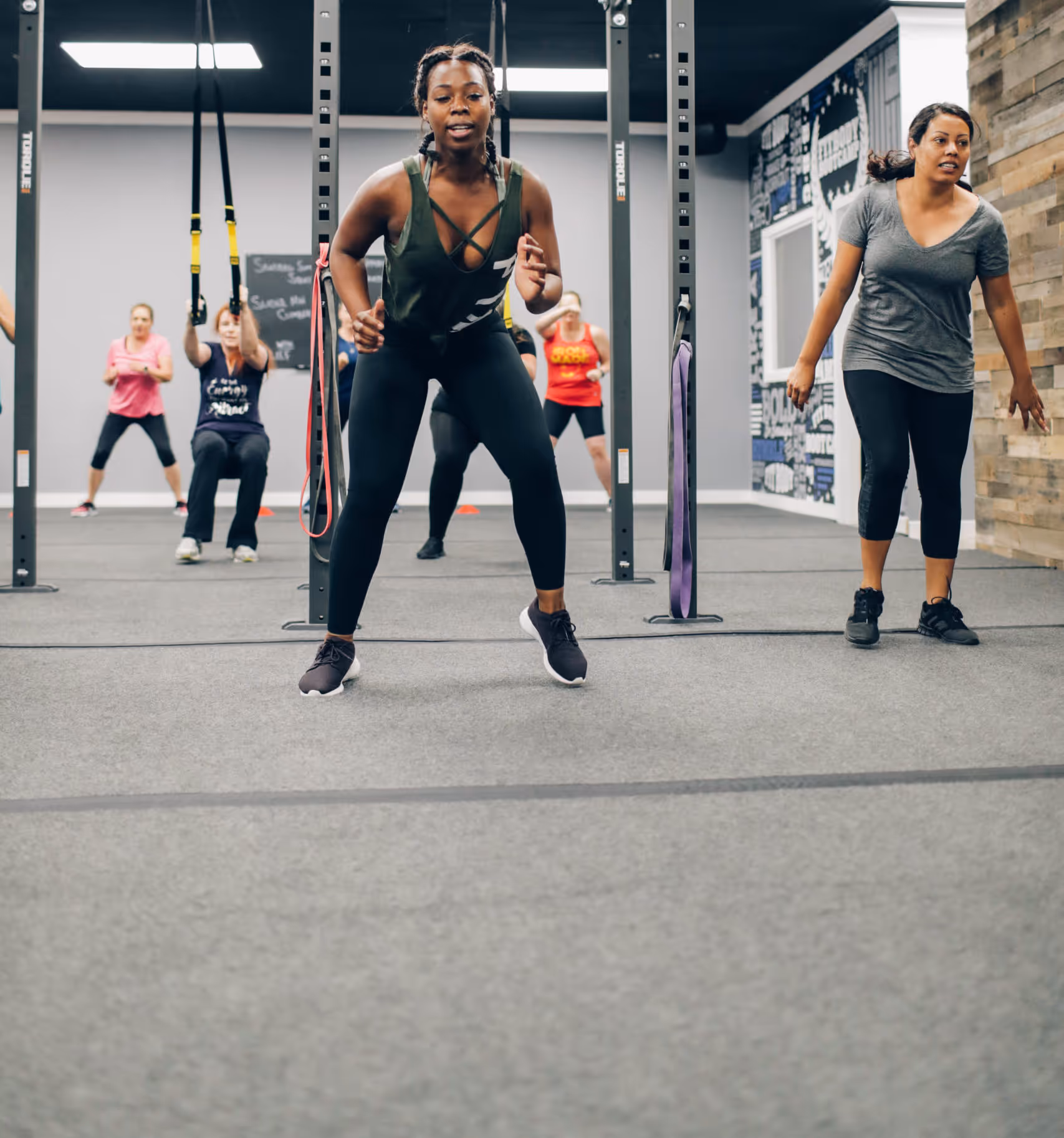 Group fitness class with women exercising in a gym using TRX straps and bodyweight movements.