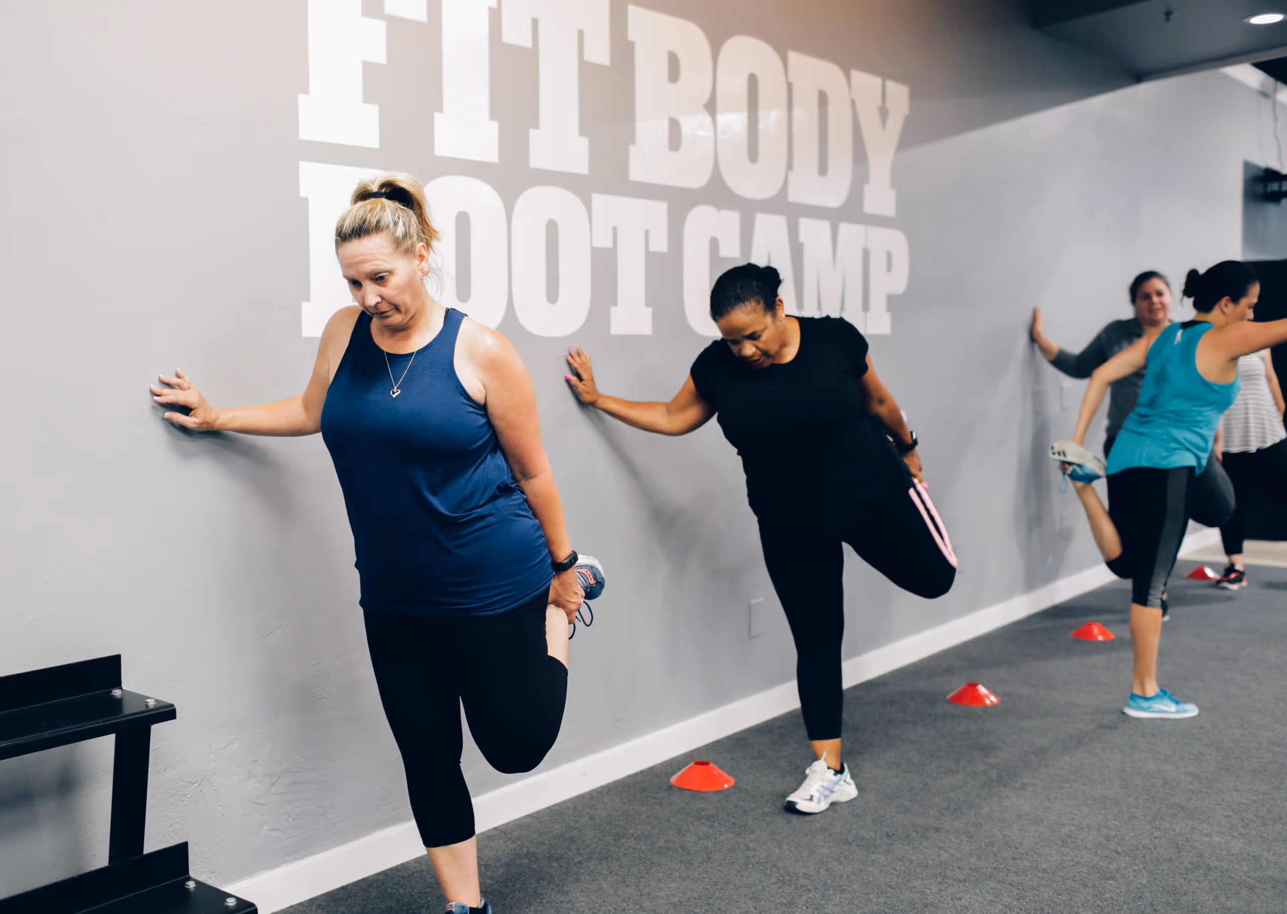 Group of women in workout clothes stretching their legs against a wall in a fitness boot camp.