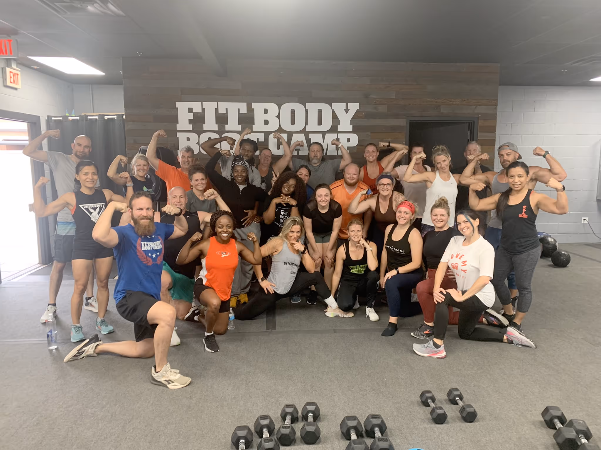 Group of diverse people posing with flexed arms inside Fit Body Boot Camp gym.