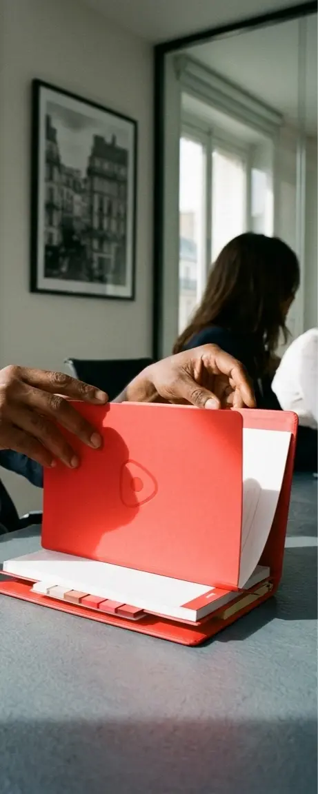Mains ouvrant un conférencier rouge personnalisé avec logo ton sur ton, dans un bureau lumineux — LOGOBJET