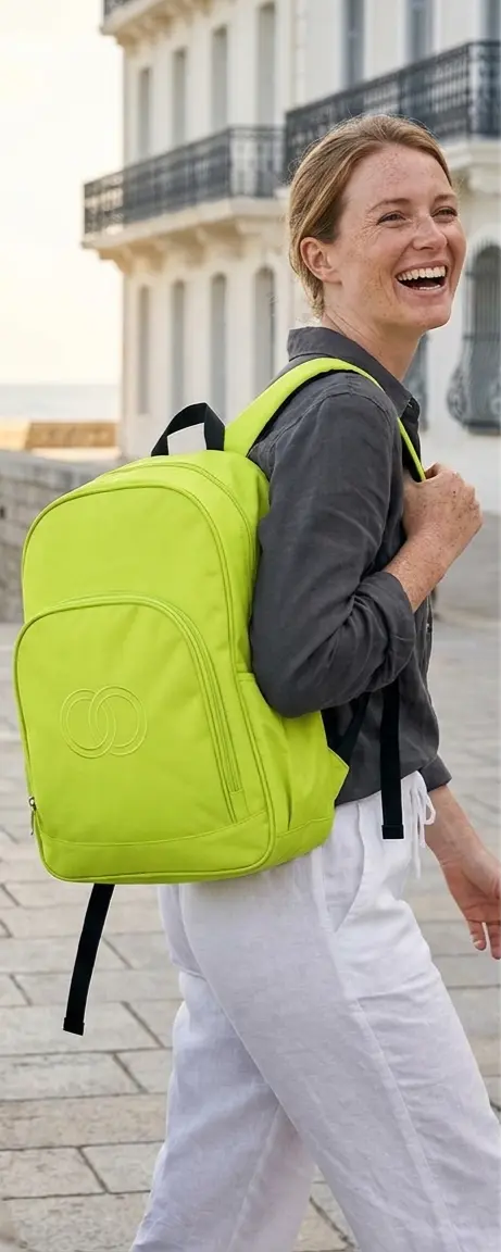Femme souriante portant un sac à dos vert anis personnalisé avec logo embossé, en bord de mer — LOGOBJET