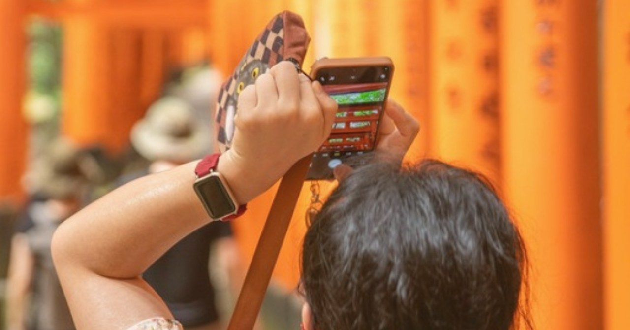 鳥居の前でスマートフォンを構える旅行者