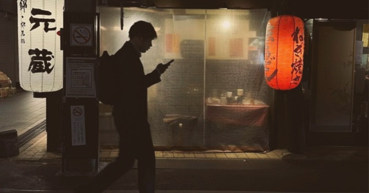 夜の飲食街でスマートフォンを見る人