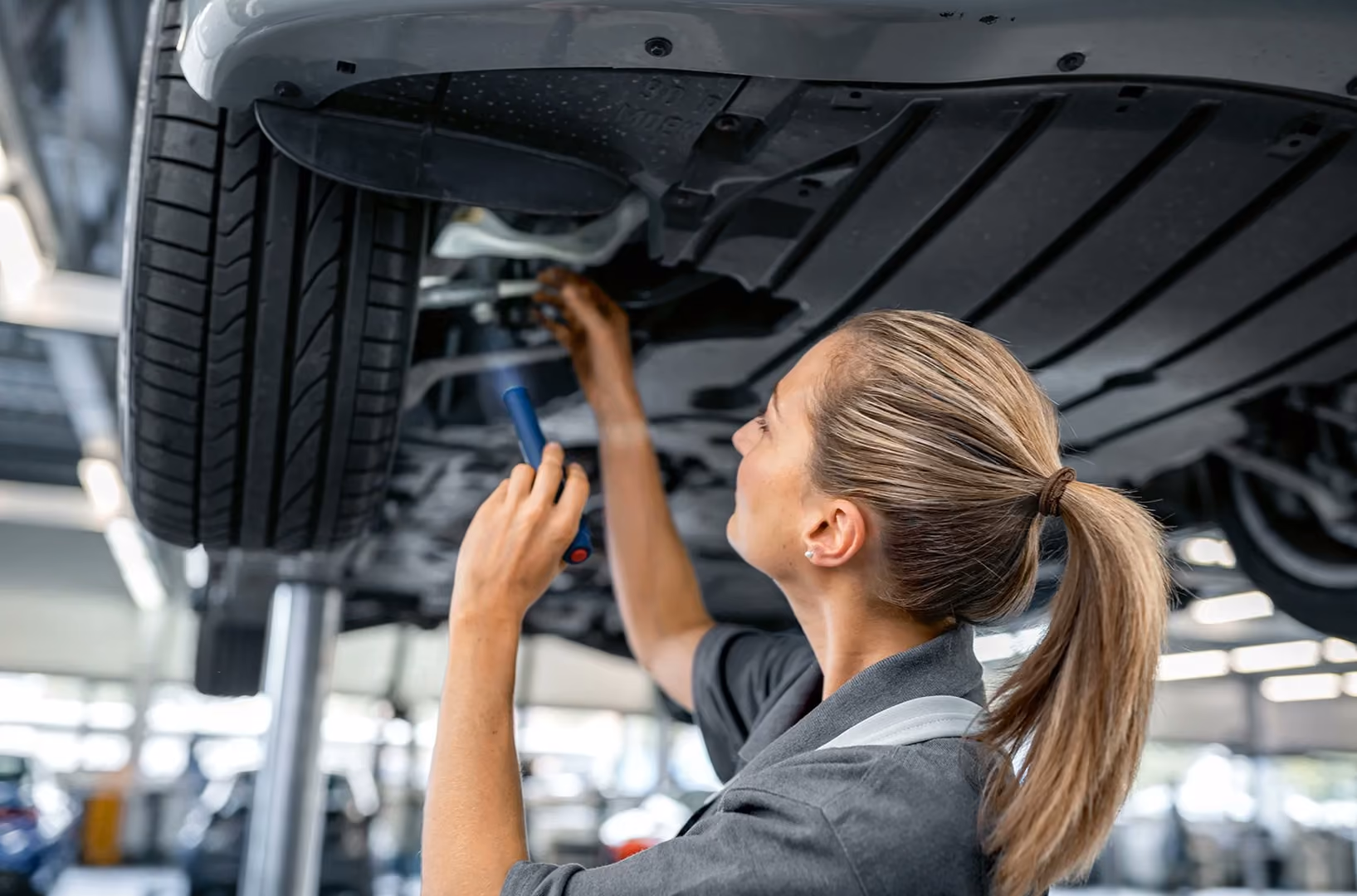Mechanic using a tool to inspect the underside of a car raised on a lift in a service garage - NetSuite for Professional Service