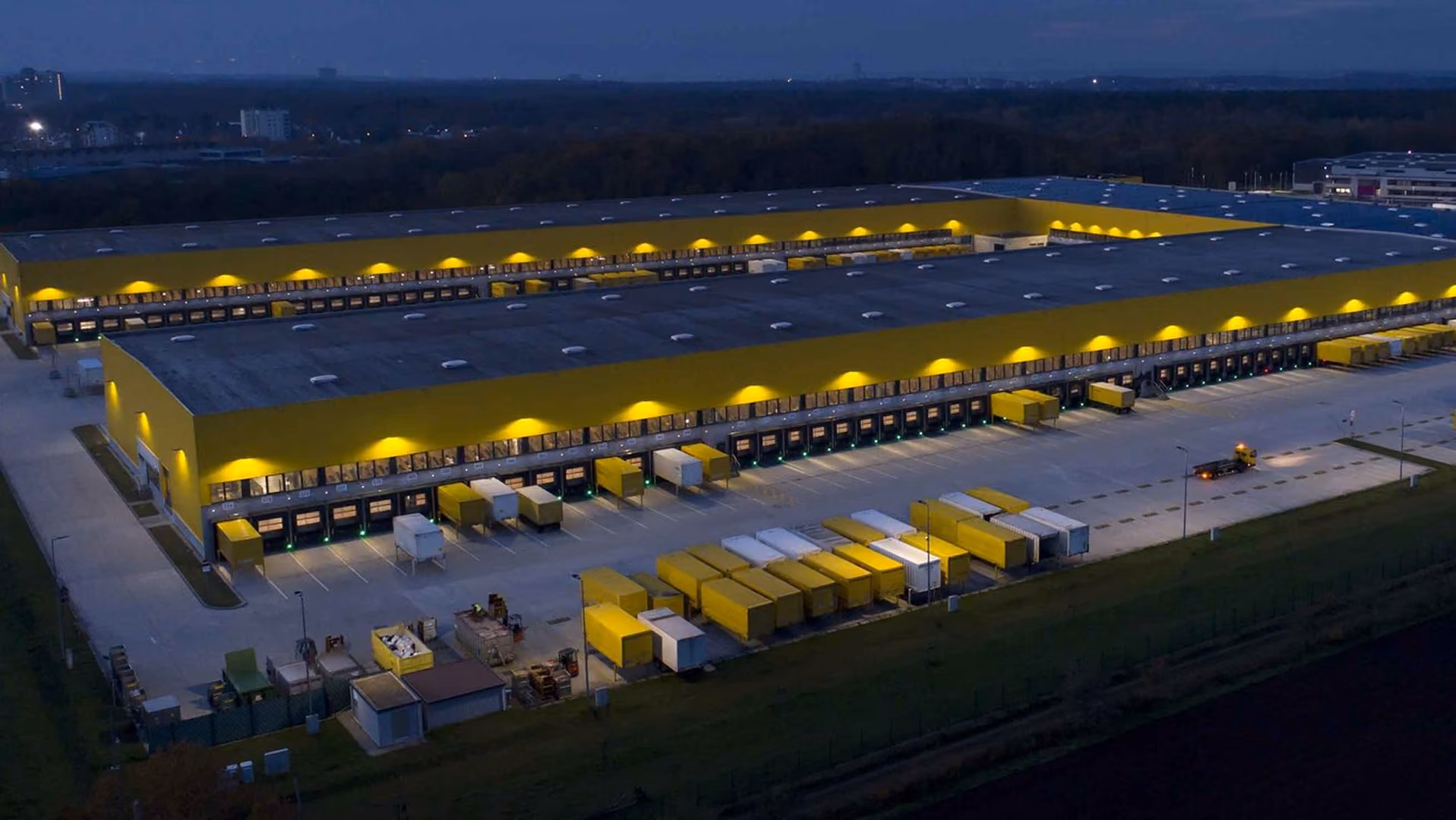 Aerial view at dusk of a large distribution center with lit loading docks and rows of trailers parked in the yard - NetSuite for wholesale distribution