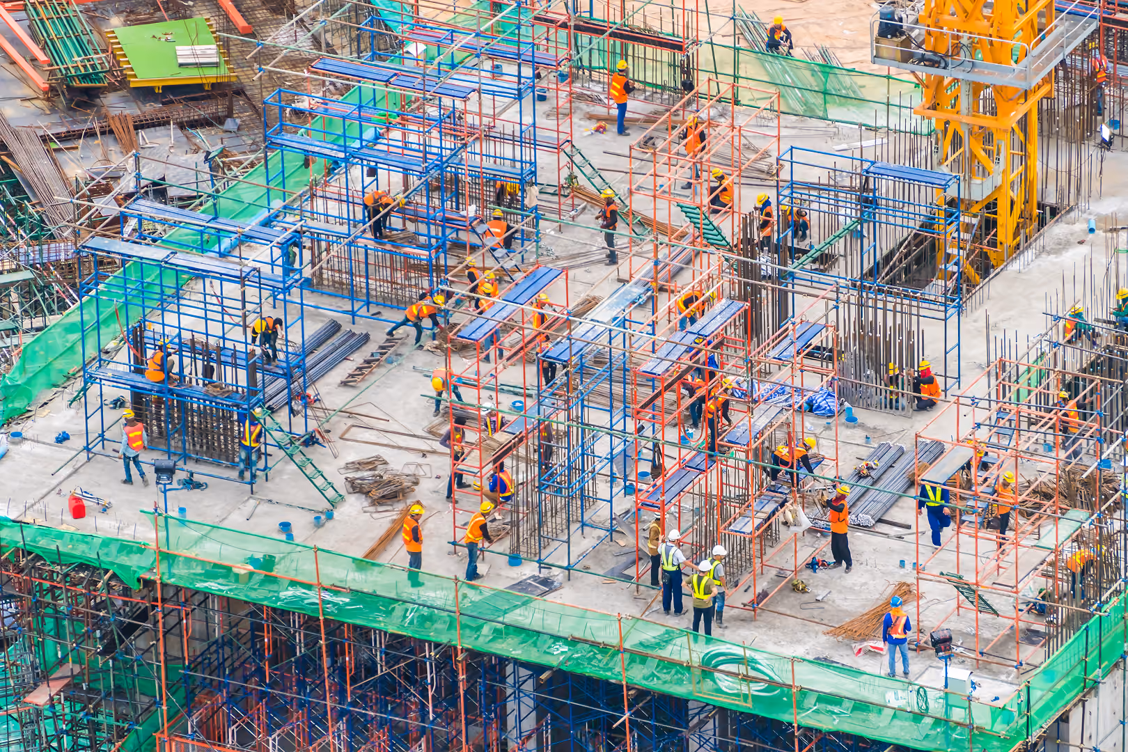 Aerial view of workers in hard hats and safety vests among scaffolding and rebar on a building deck under construction - NetSuite for Construction