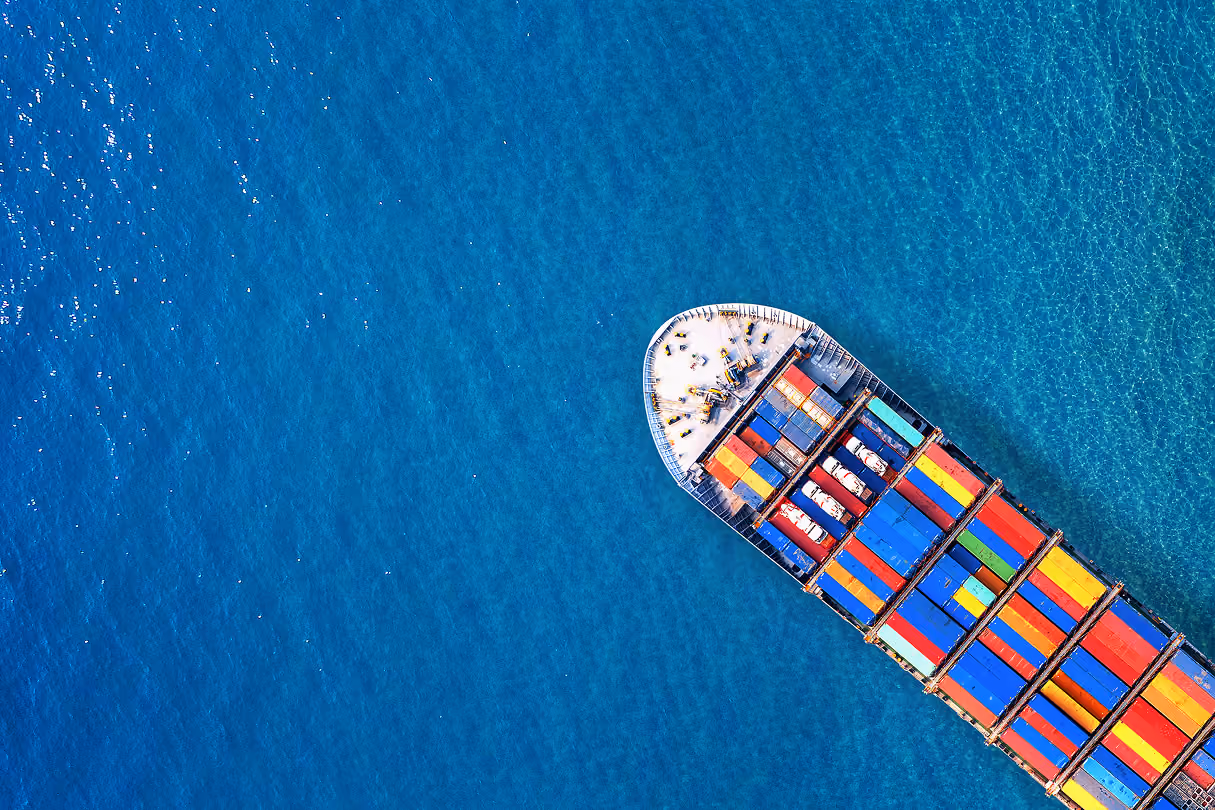 Aerial view of a cargo ship loaded with colorful shipping containers crossing deep blue open water - NetSuite for Logistics