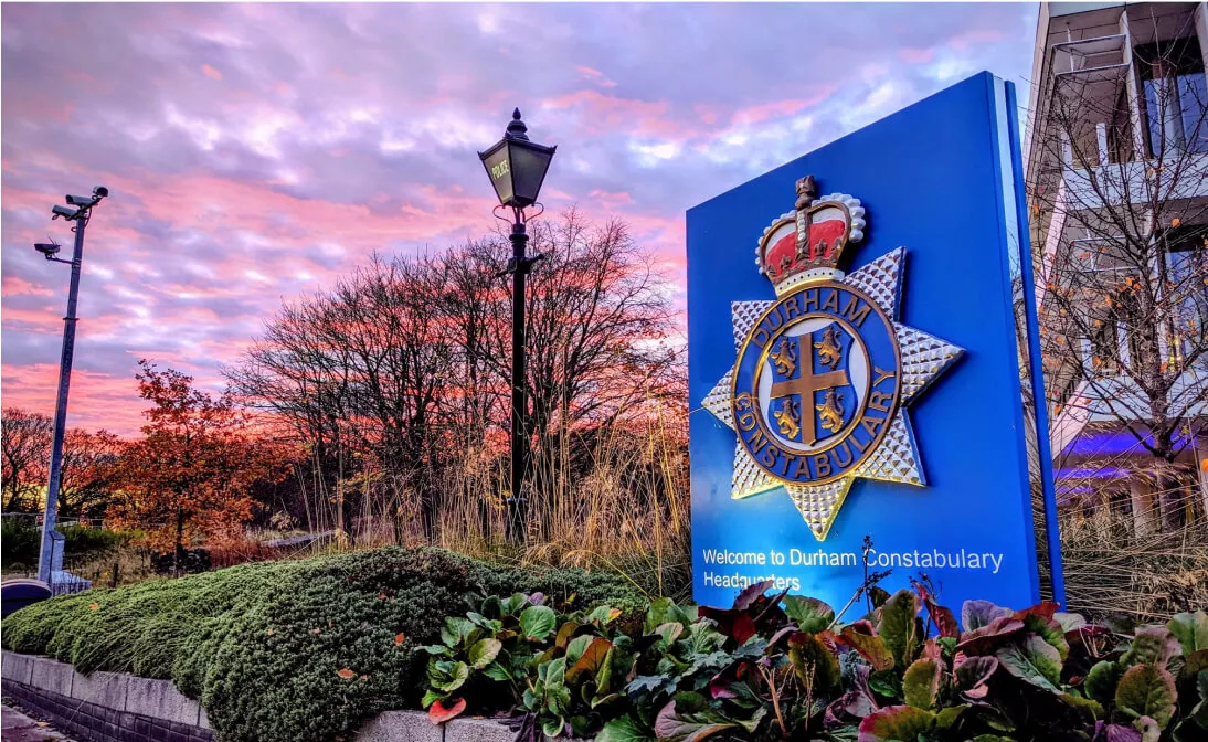 Durham Constabulary Headquarters sign at sunset with trees, plants, and a lamp post visible.