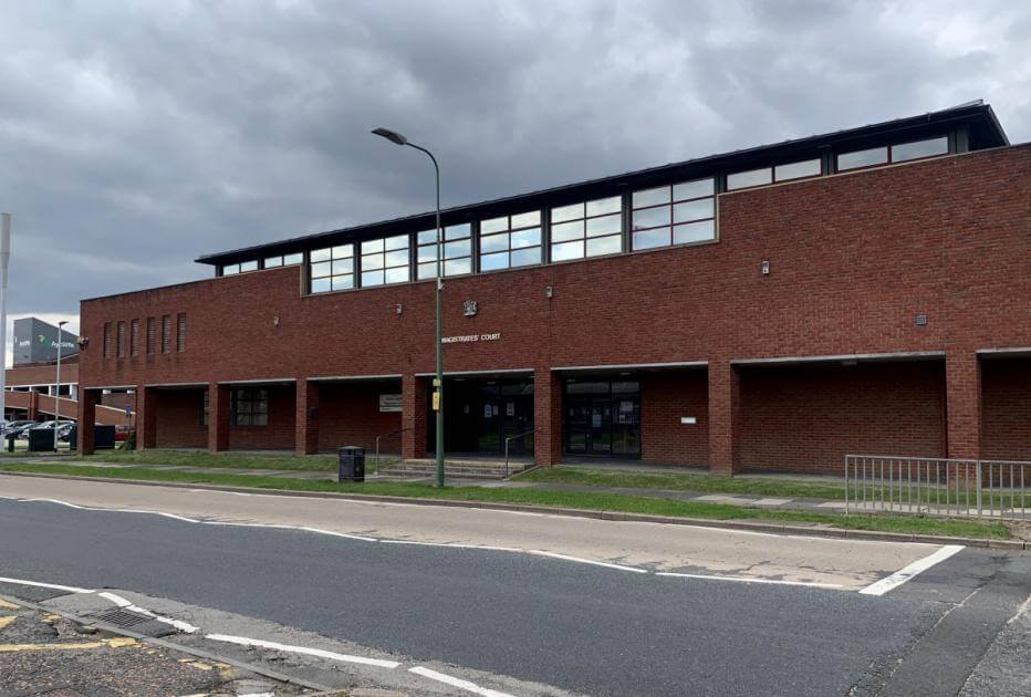Red brick building labeled Magistrates' Court under a cloudy sky, with a road and sidewalk in front.