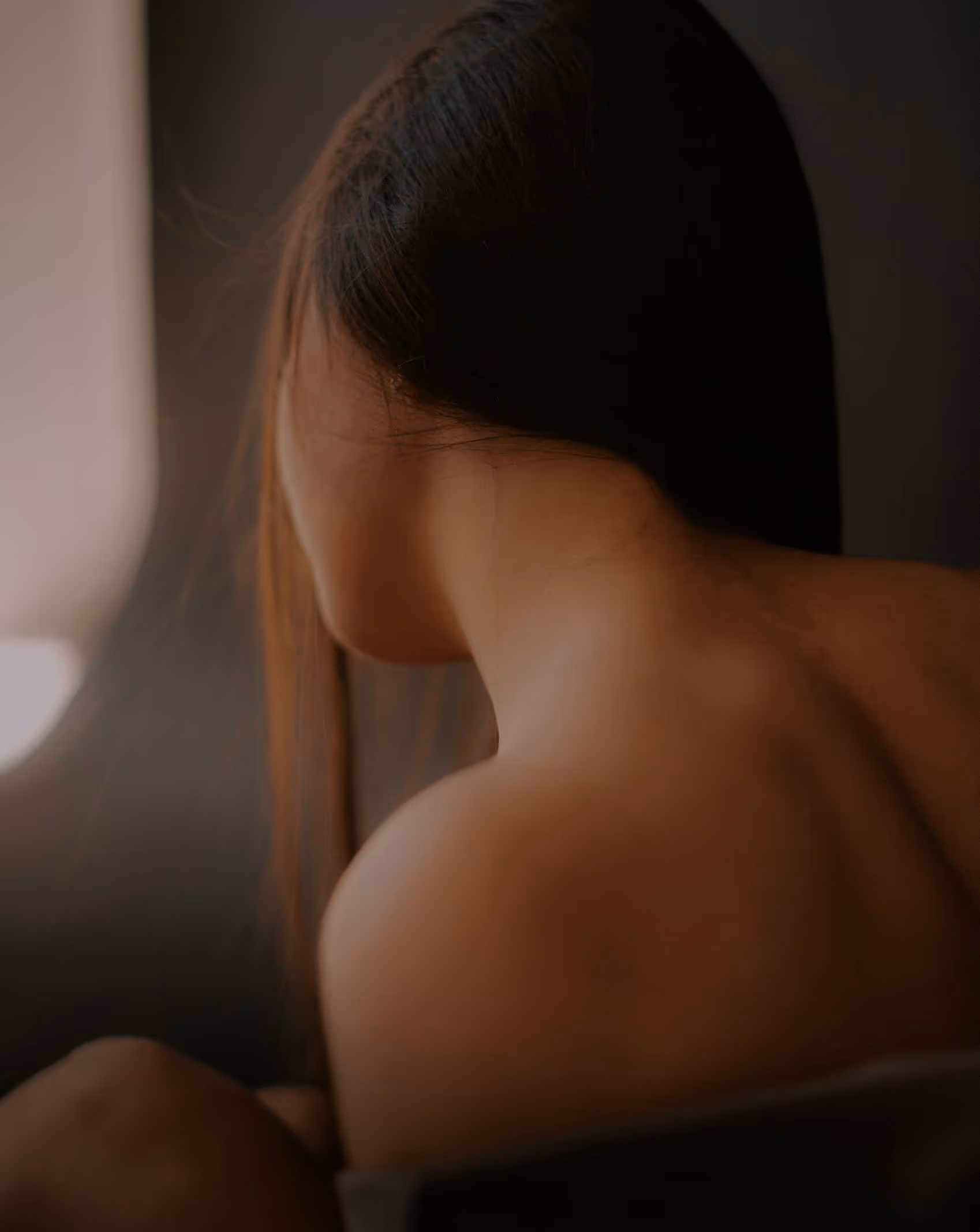 Close-up of a woman's bare shoulder and neck with dark hair against a soft background.