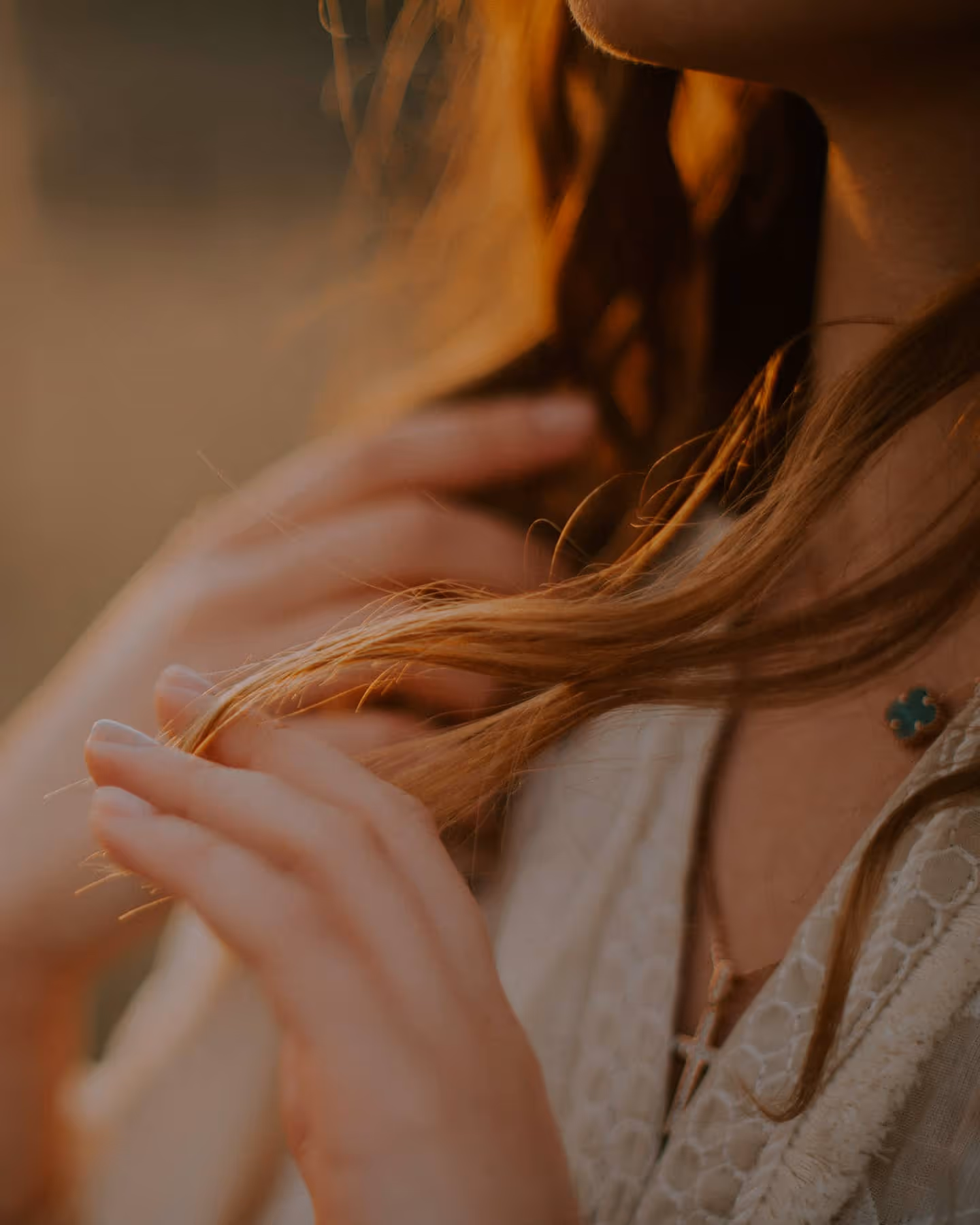 Close-up of a person touching their long hair near their neck with a cross necklace visible.