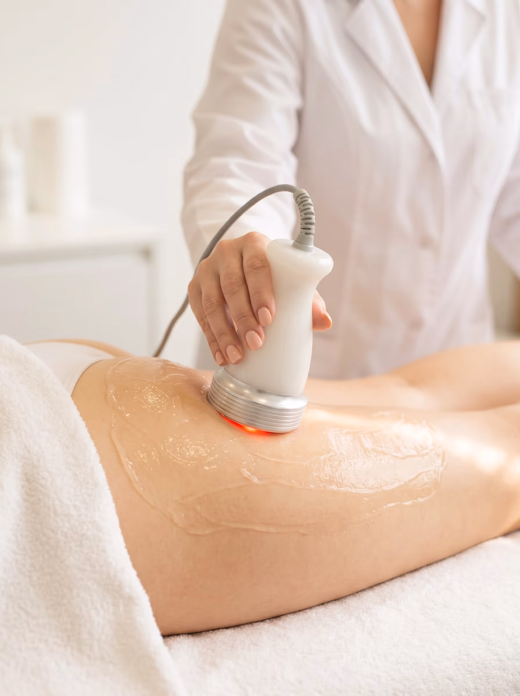 Eine Person erhält eine Schönheitsbehandlung am Bein mit einem Handgerät und Gel.