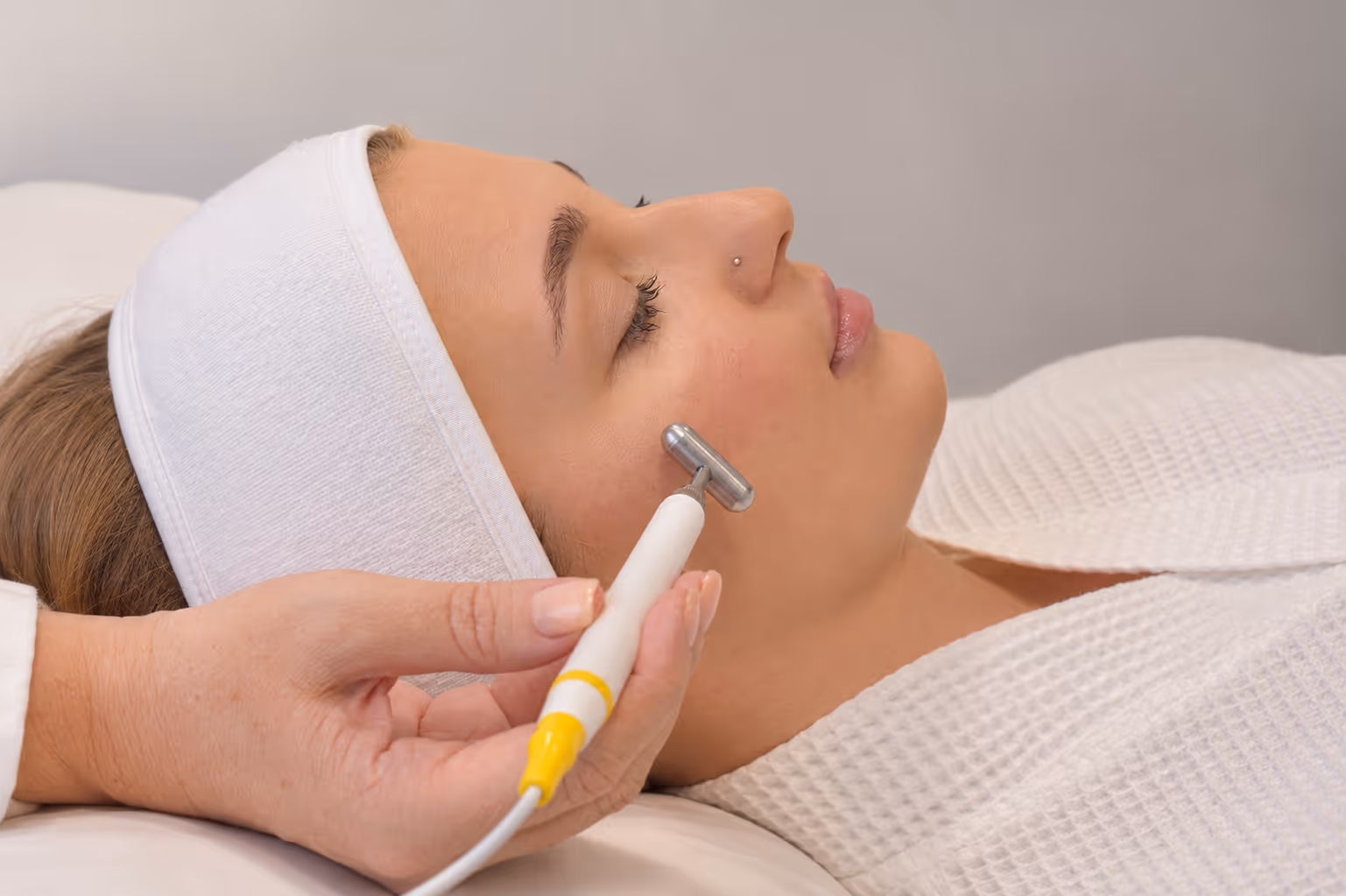 Frau mit weißem Stirnband erhält eine Gesichtsmassage mit einem Metallroller im Spa.