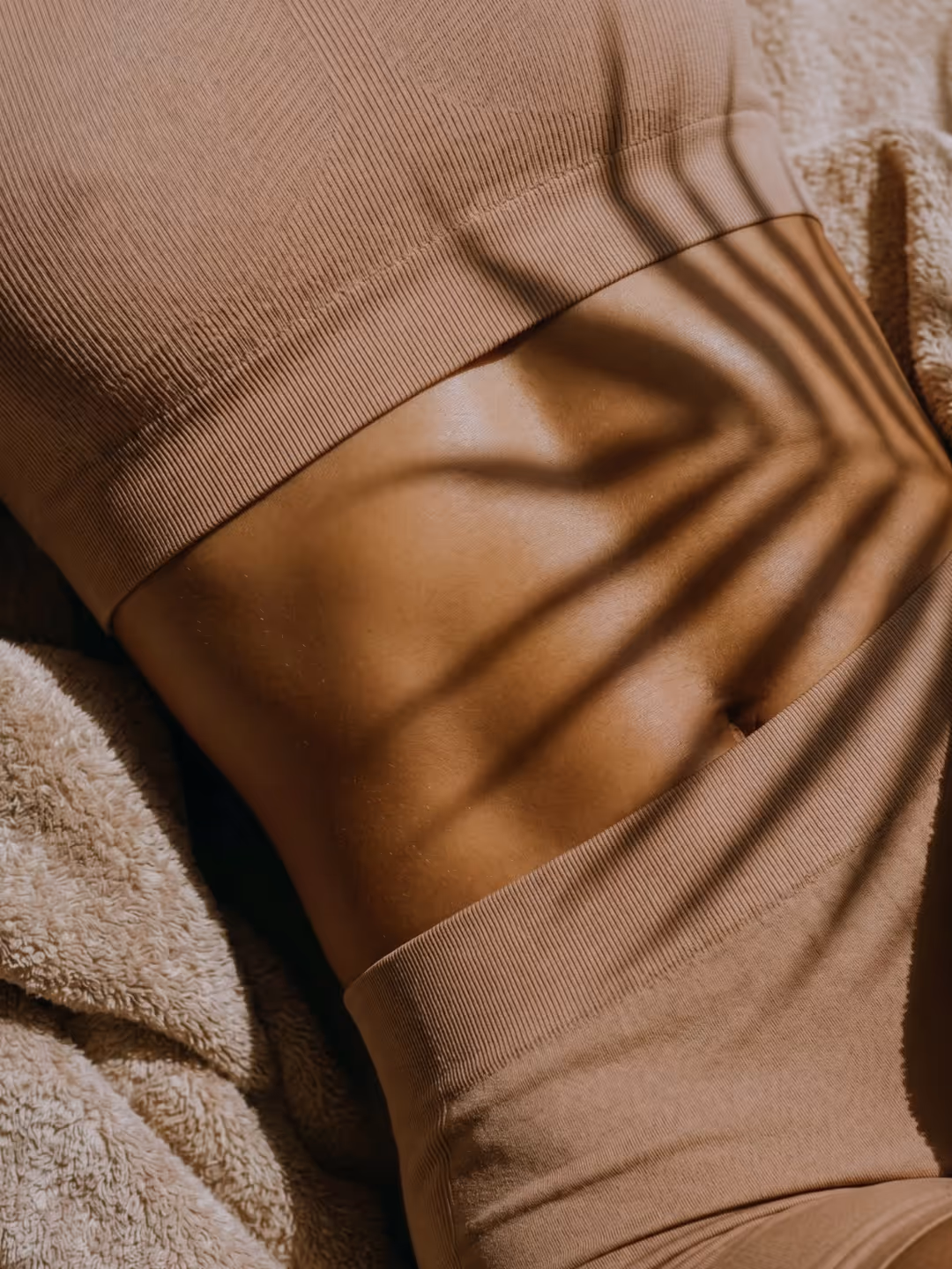 Nahaufnahme von Bauch und Taille einer Person in beiger Kleidung mit Schatten einer Pflanze.