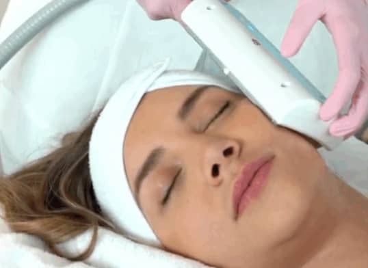 Frau mit geschlossenen Augen erhält Gesichtsbehandlung mit Gerät durch Handschuhe.
