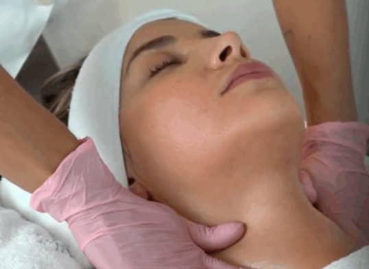 Frau mit geschlossenen Augen erhält Nackenmassage von Händen mit rosa Handschuhen.