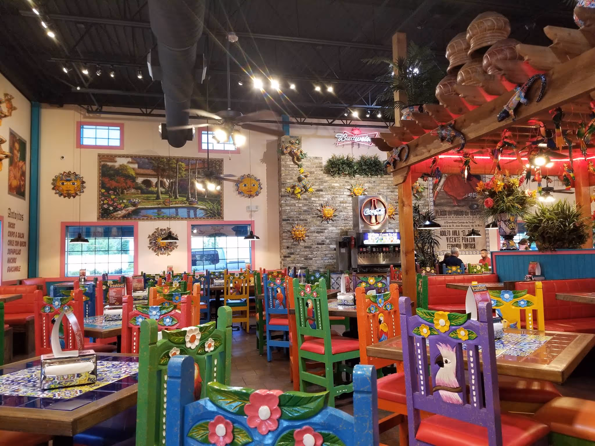 Colorful Mexican restaurant interior with hand-painted chairs, tiled tables, and festive wall décor.