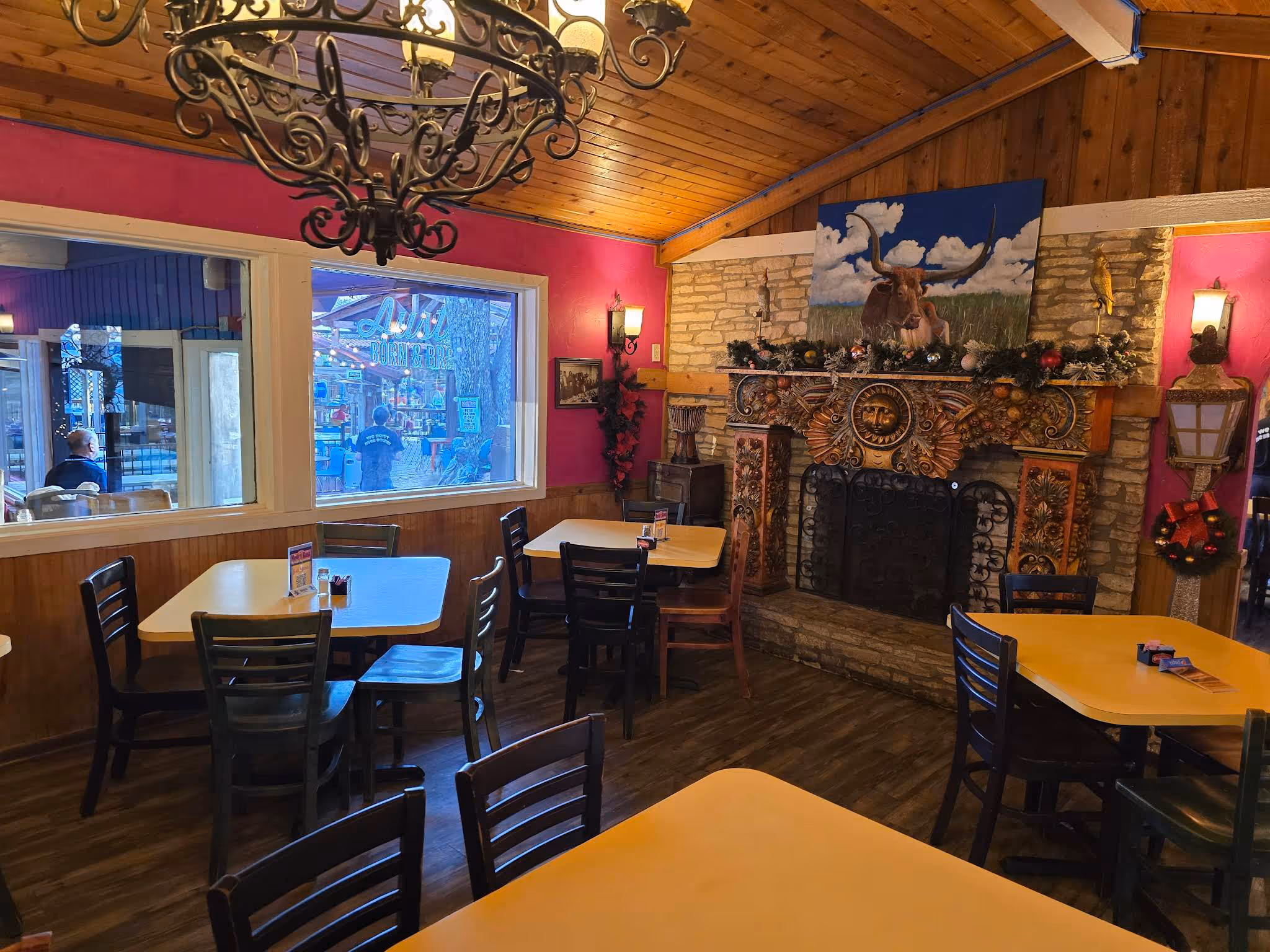 Restaurant interior with yellow tables, black chairs, a decorated fireplace, and a painting of a longhorn bull.