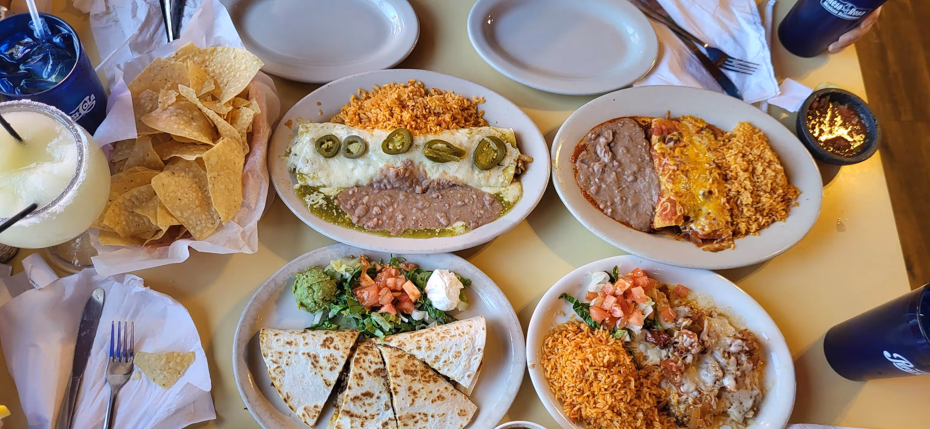 Table with Mexican food including chips, margarita, rice, beans, enchiladas, and quesadillas.