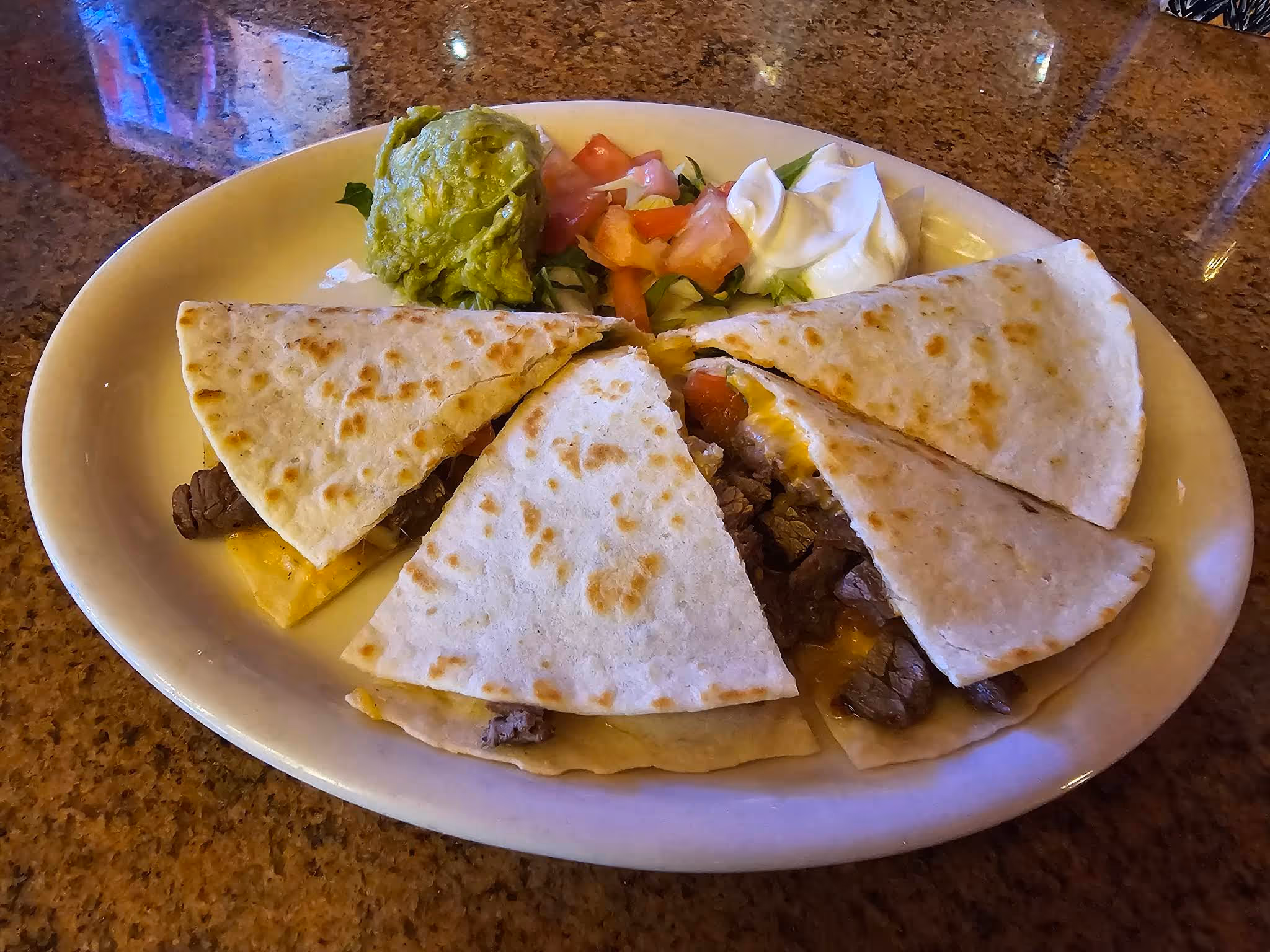 Plate with three beef and cheese quesadilla slices, guacamole, sour cream, and diced tomato salad.