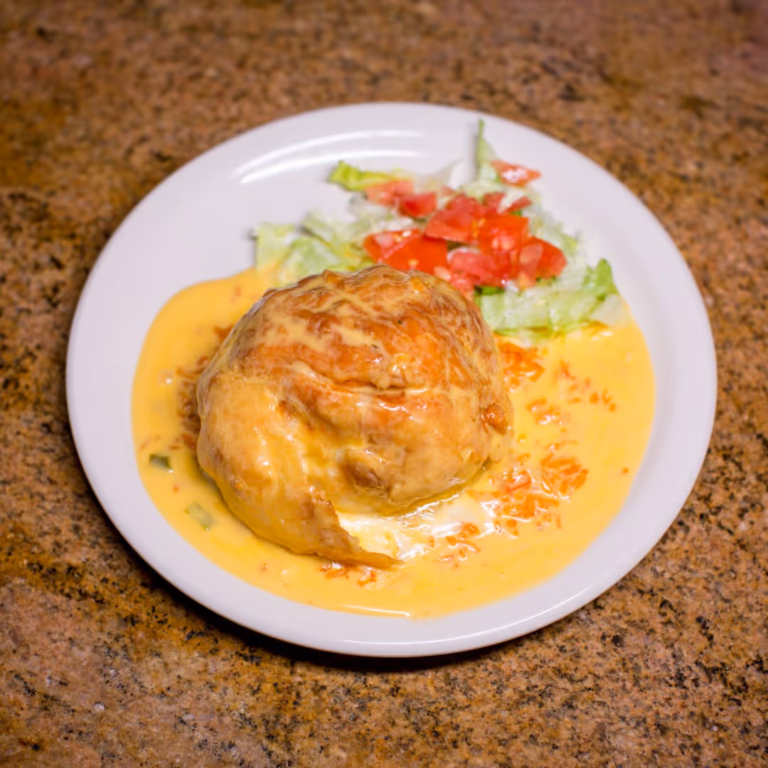 Plate with a cheese-covered fried ball, creamy sauce, and a side of lettuce and diced tomatoes.