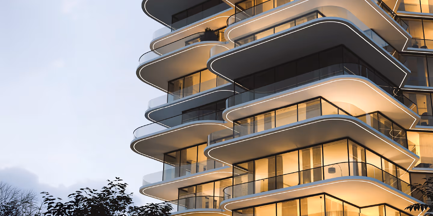 Modern building with curved balconies and glass railings glowing at dusk.