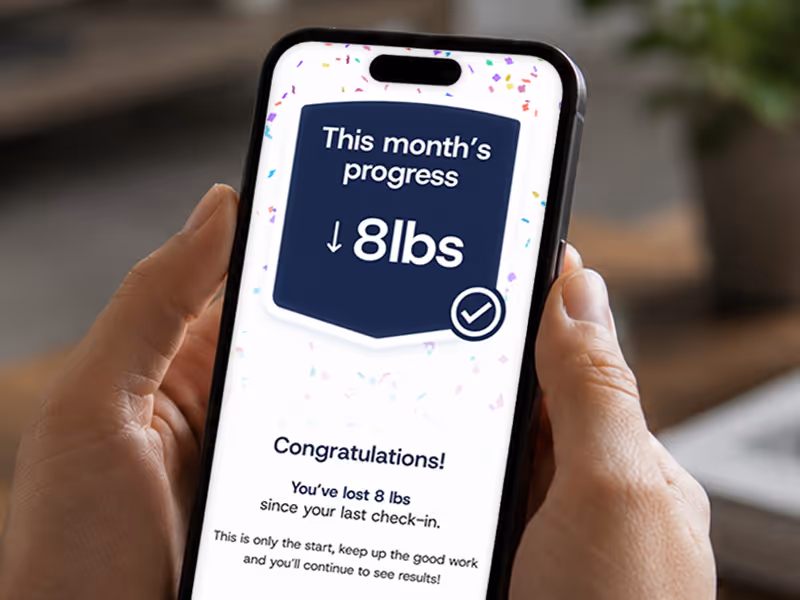 Smartphone showing weight loss app with message: This month's progress down 8 lbs, congratulations.