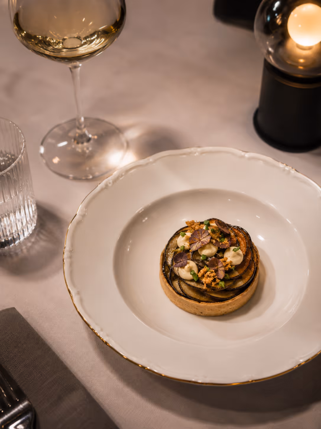 Gourmet tart with layered vegetables and cream garnished with herbs on white plate.