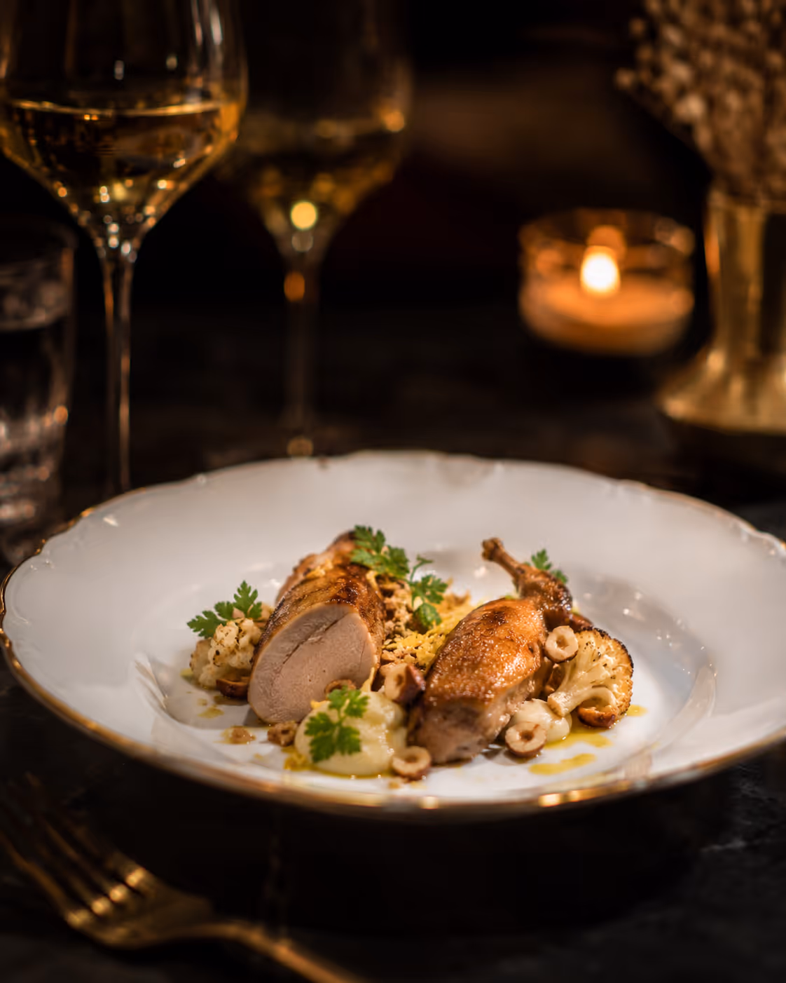 Plated gourmet duck breast and leg with cauliflower, hazelnuts, and herbs on white dish.
