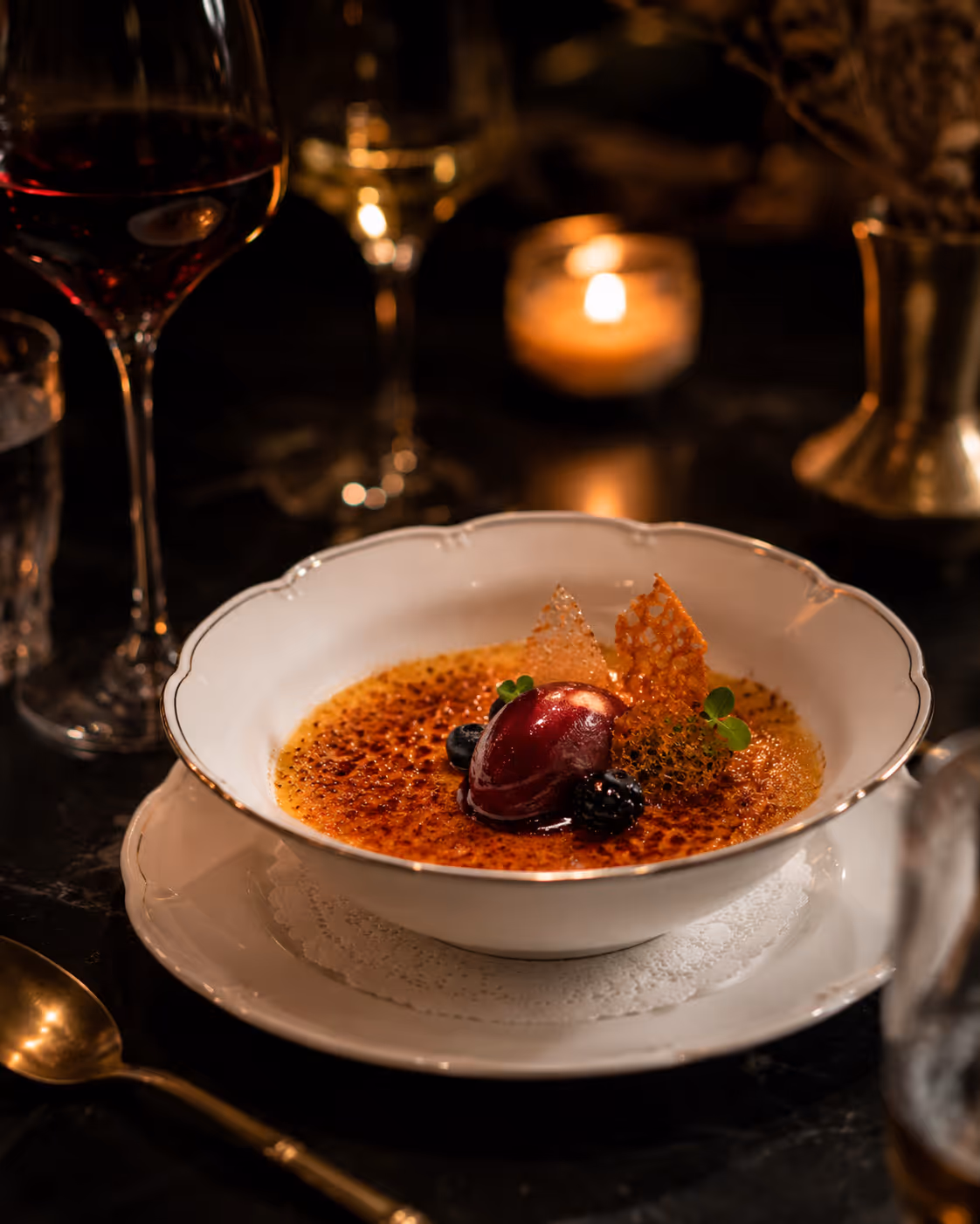 Creme brûlée dessert with berry sorbet, blackberries, and caramel crisps in a white bowl on a plate.