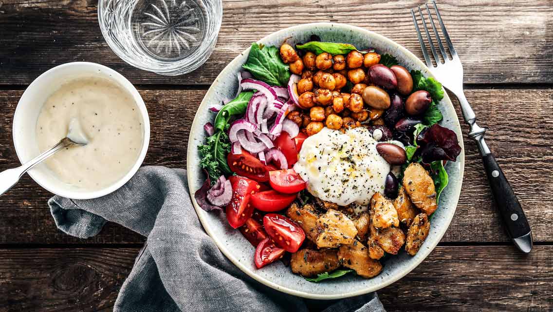 A bowl with lots of veggies, plant based chicken, chickpepas and a dip.