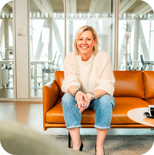 Gabriele Bahner sitzt auf einem orangefarbenen Sofa im Büro.