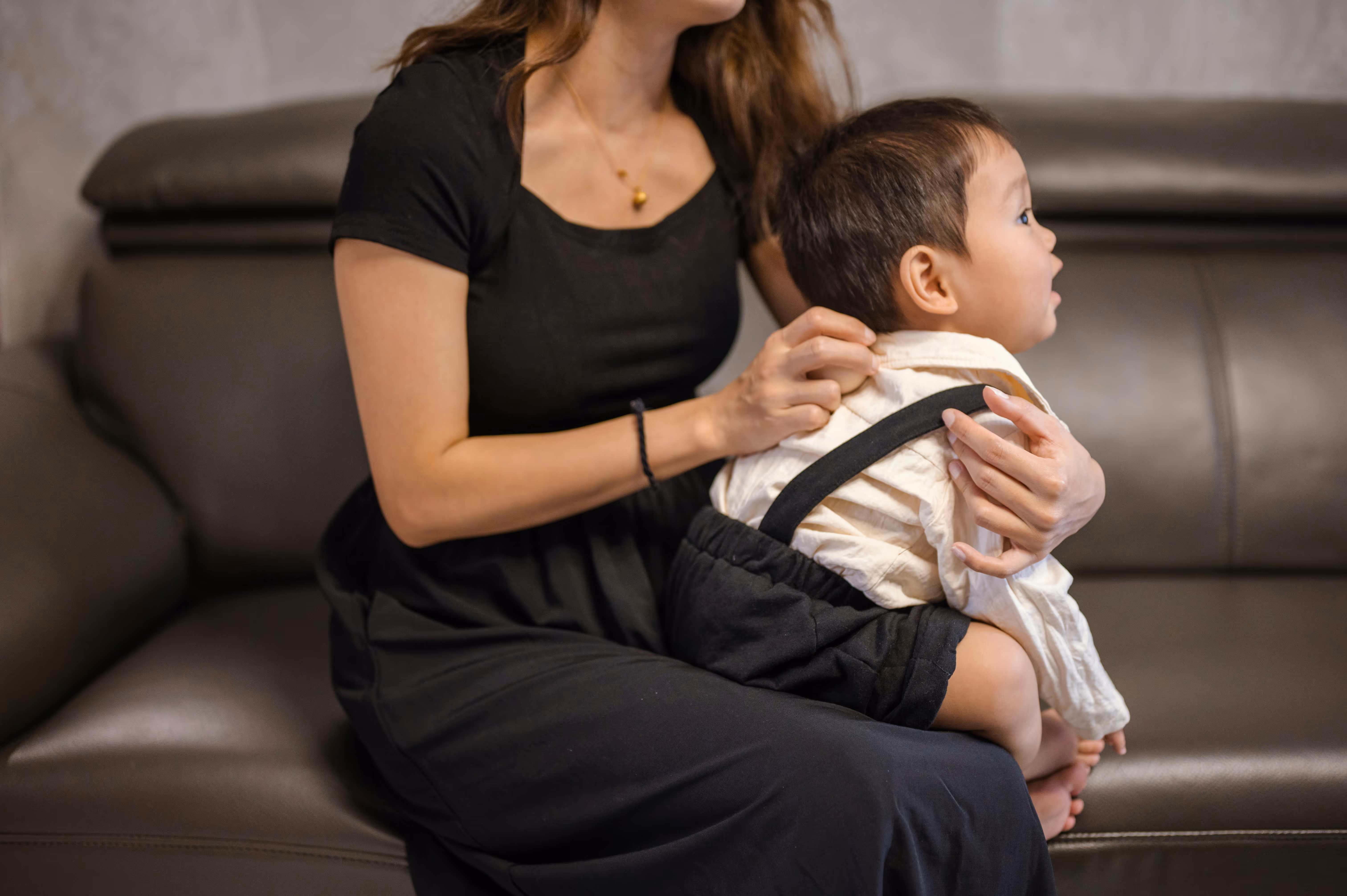 A grayscale image of a mother sitting on a couch and holding an infant looking off to the right.