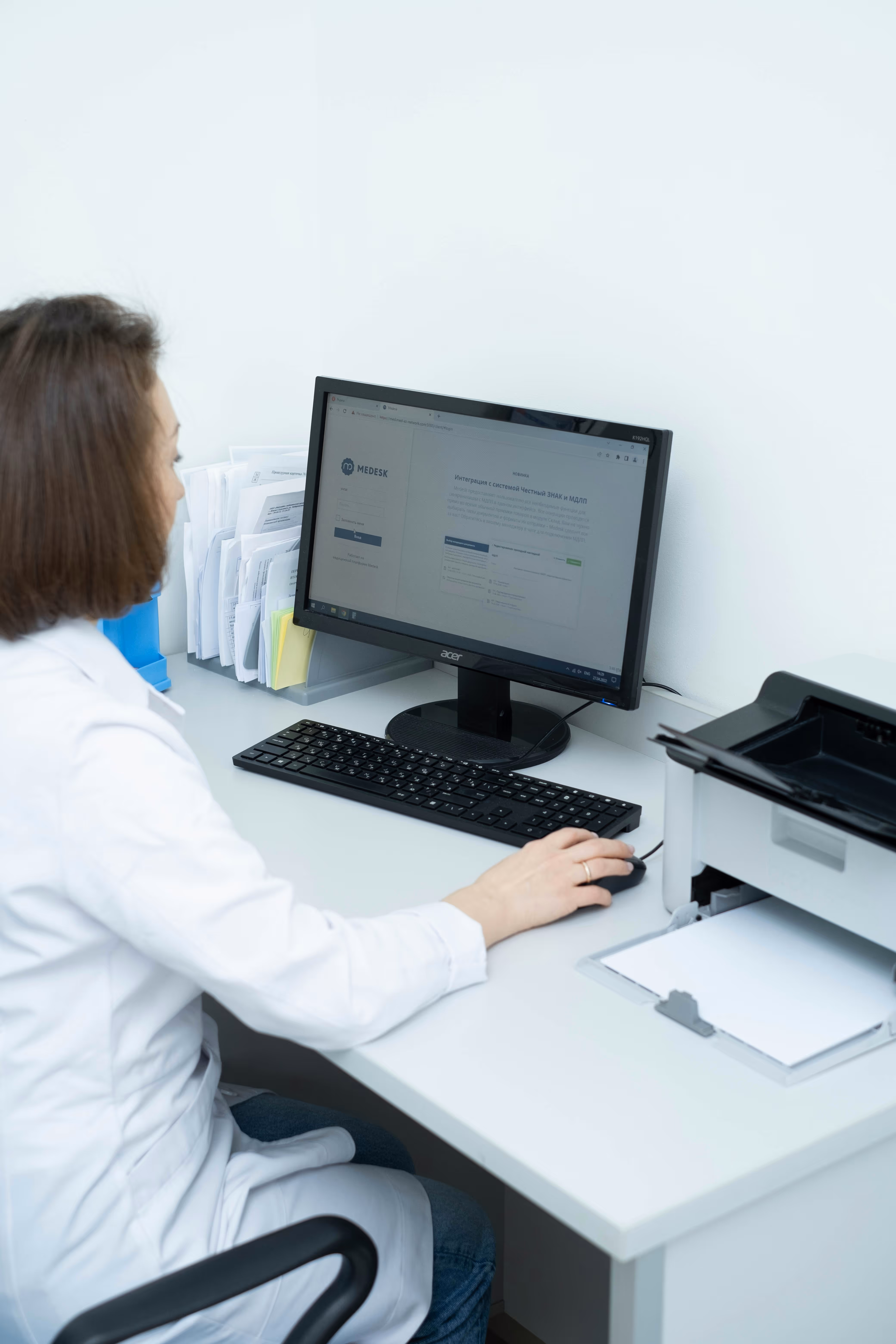 A doctor sitting at a desk doing work on a computer with her back to the viewer