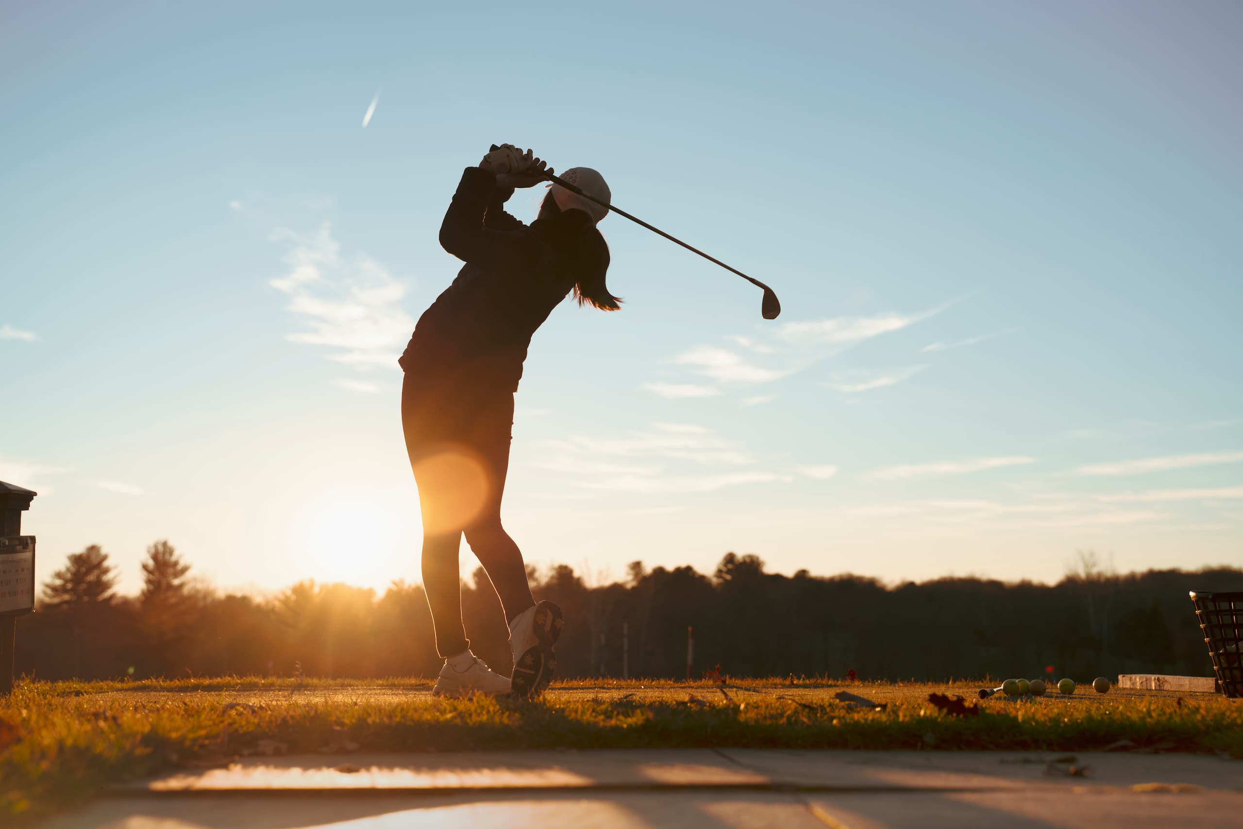 Young female golfer driving from tee silhouetted at sunrise/sunset.