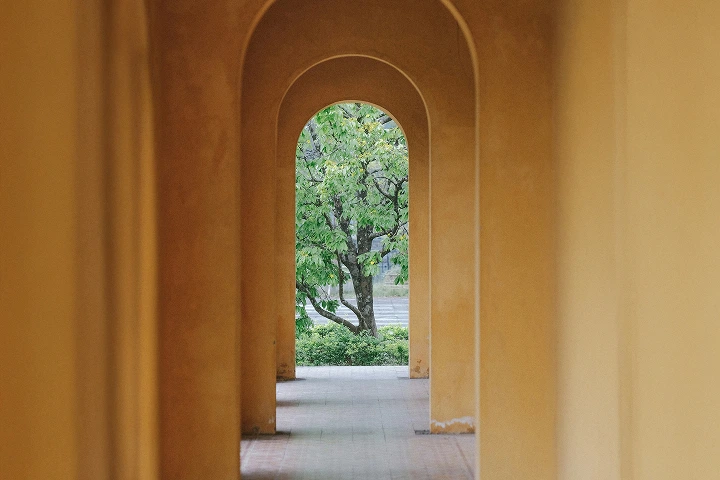 Archway corridor with yellow walls framing green leafy trees at the end outdoors.