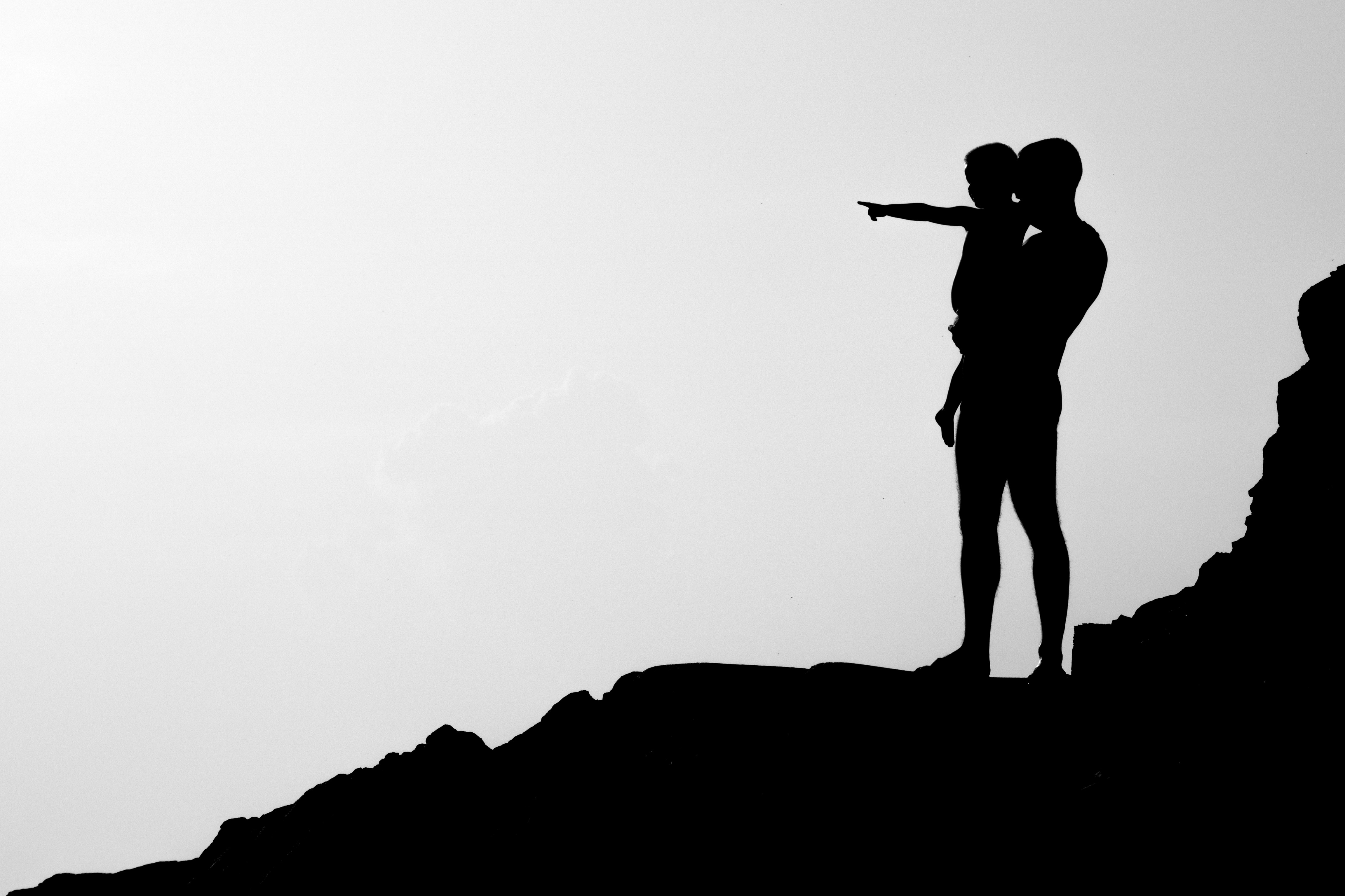 Silhouette of an adult holding a child who is pointing while standing on rocky terrain.