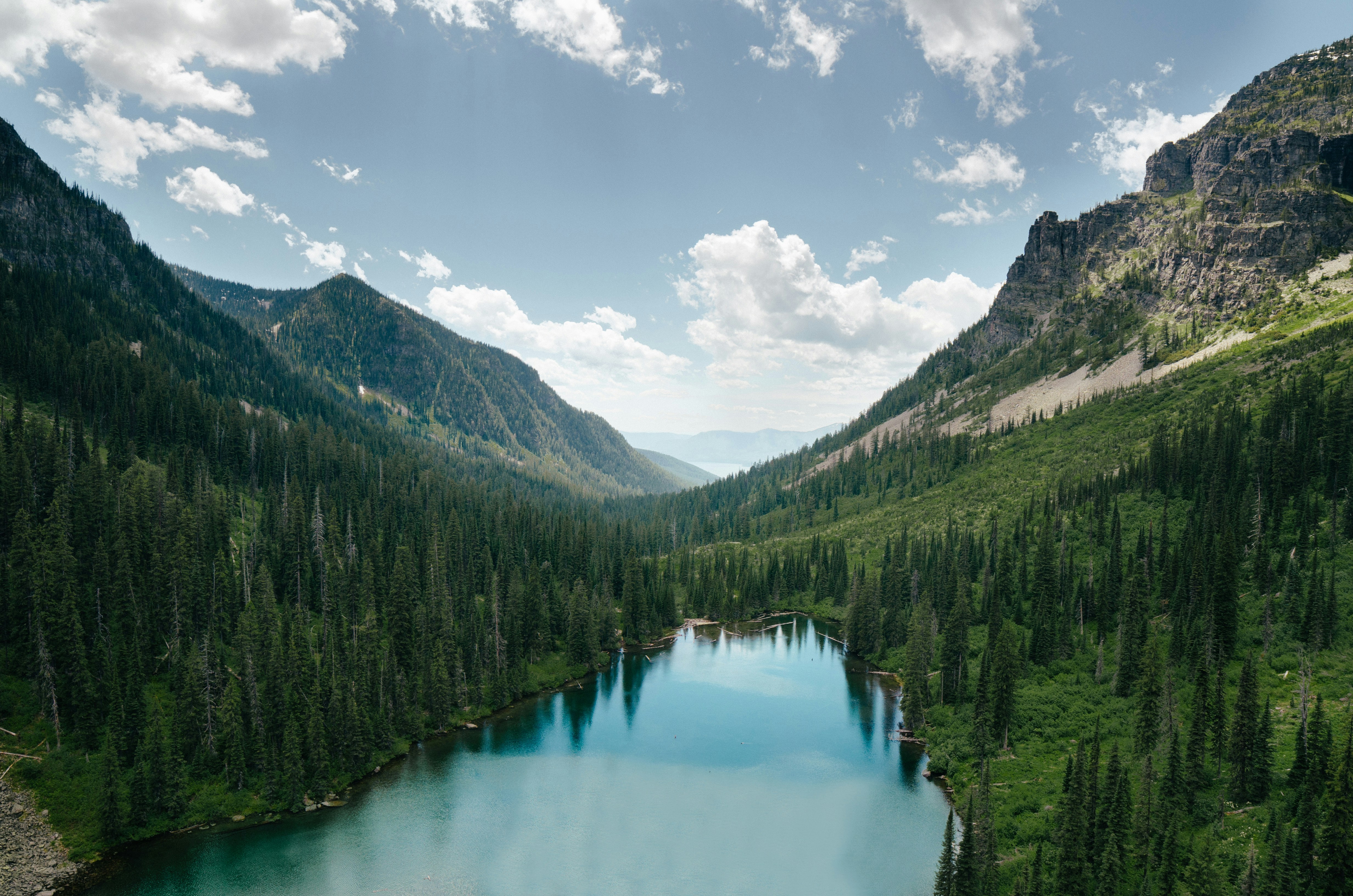 Serene mountain lake surrounded by dense pine forests and rocky hills under a partly cloudy sky.