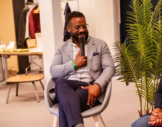 Un homme assis dans un fauteuil parlant dans un microphone lors d'un événement intérieur.