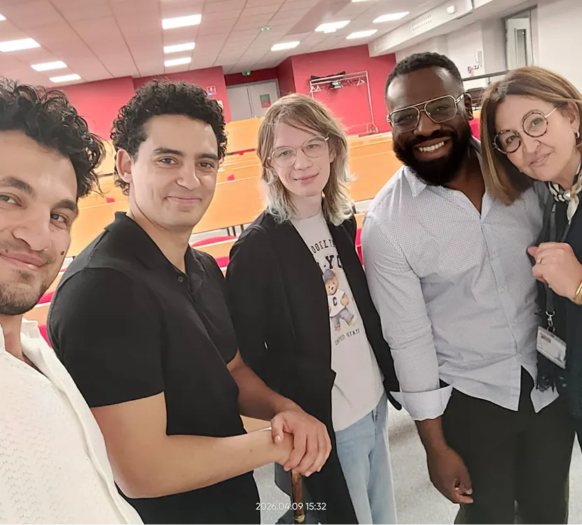 Cinq personnes souriantes posent ensemble dans une salle avec des chaises et tables.
