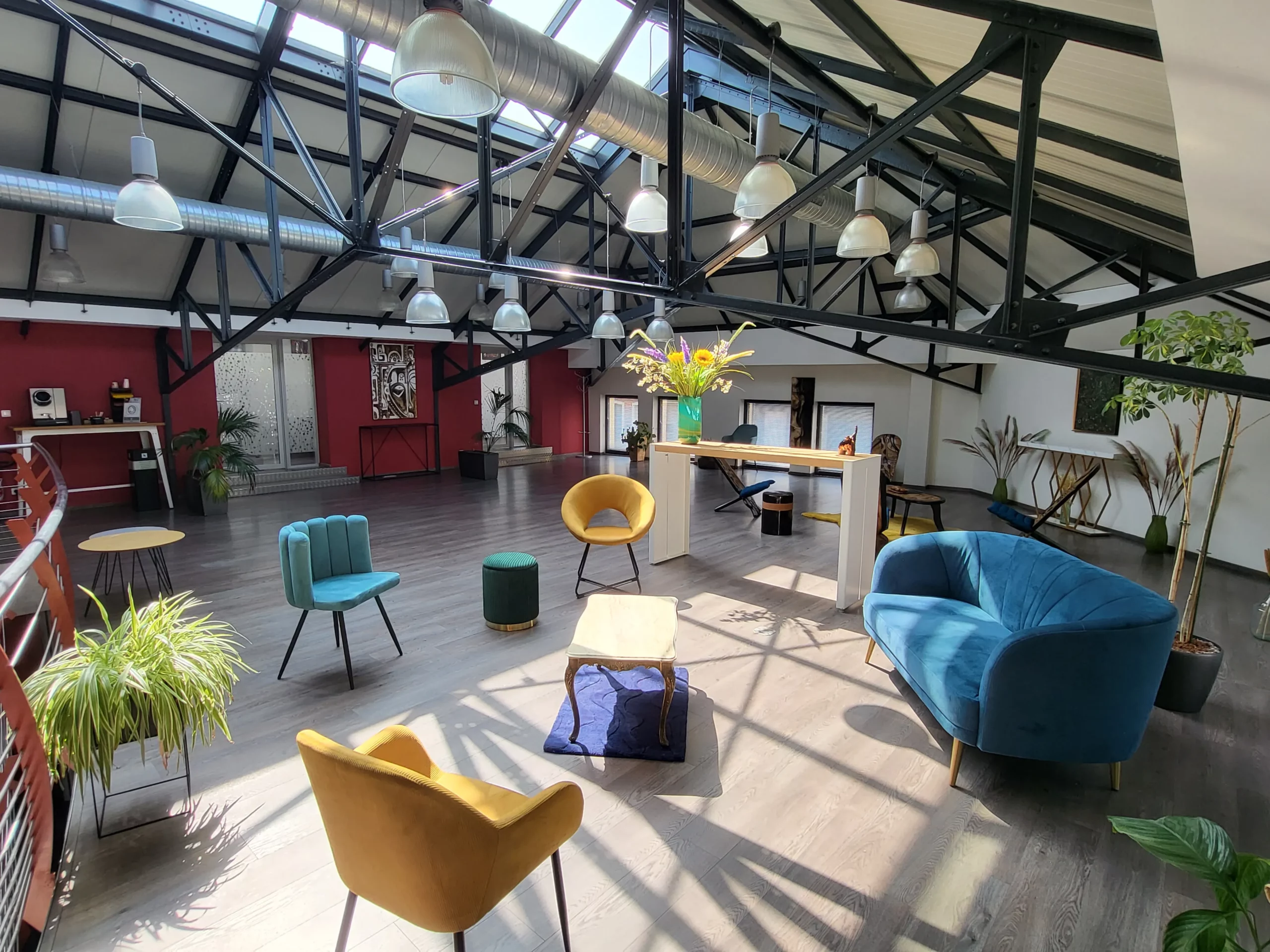 Espace lumineux avec canapés bleu et jaunes, chaises colorées, table basse, et plantes décoratives.