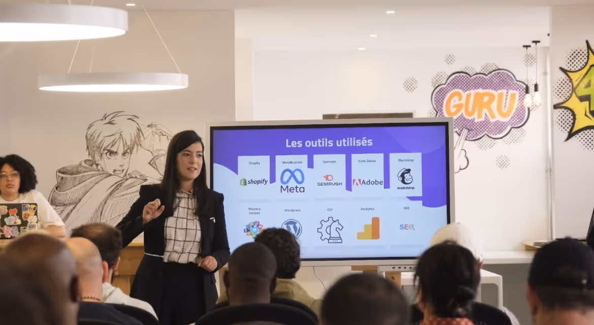 Femme présentant devant un écran montrant des outils numériques comme Shopify, Meta, Adobe à un public.