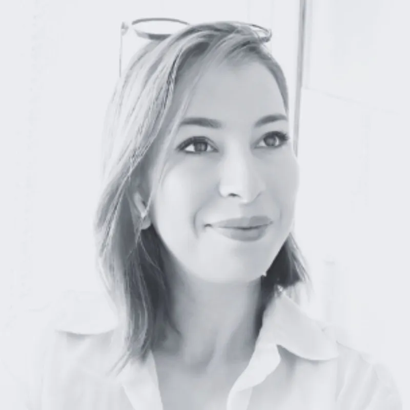 Portrait en noir et blanc d'une femme souriante avec des lunettes posées sur sa tête.
